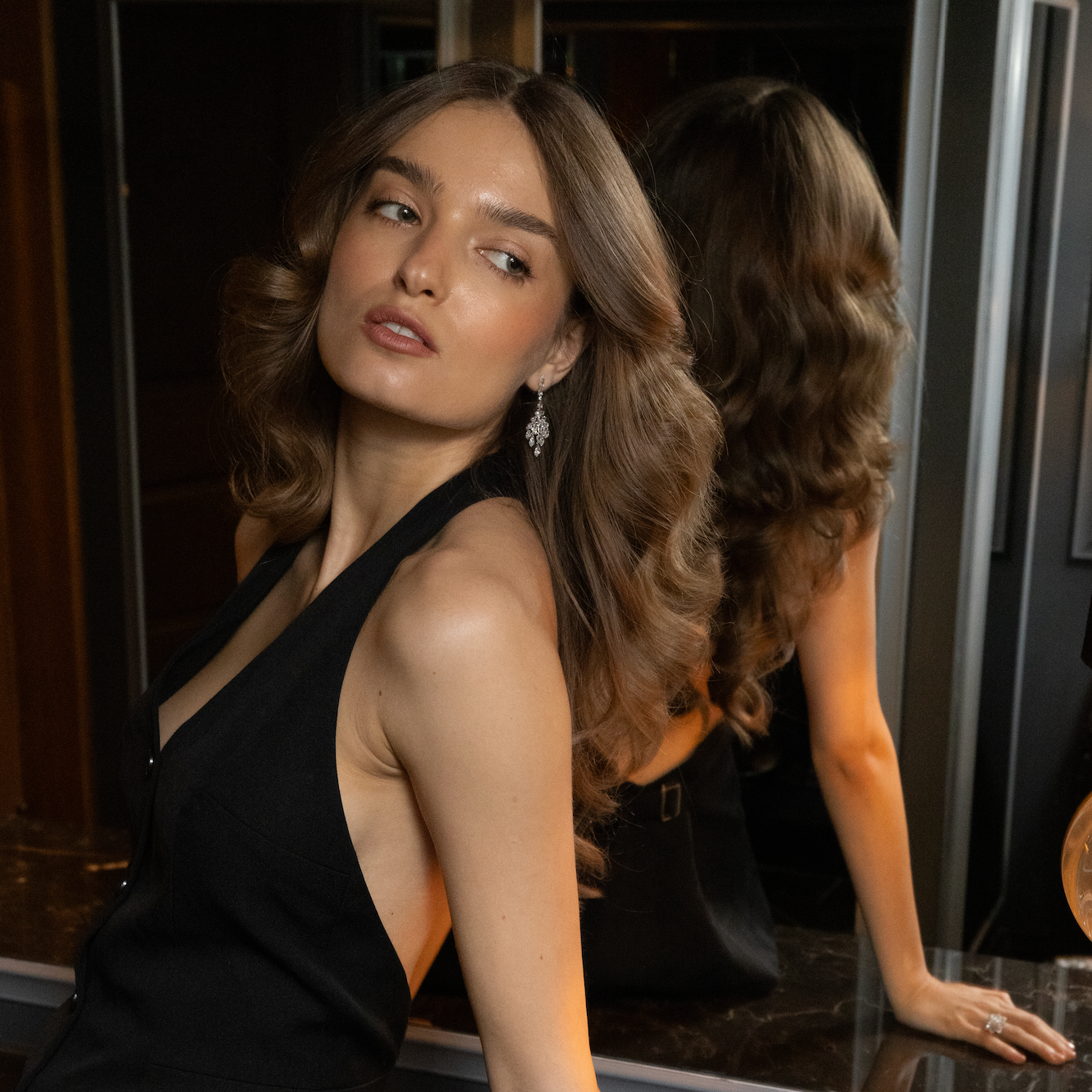 Model wearing diamond chandelier earrings in white gold, styled with an evening look and soft waves, photographed in warm, elegant lighting.