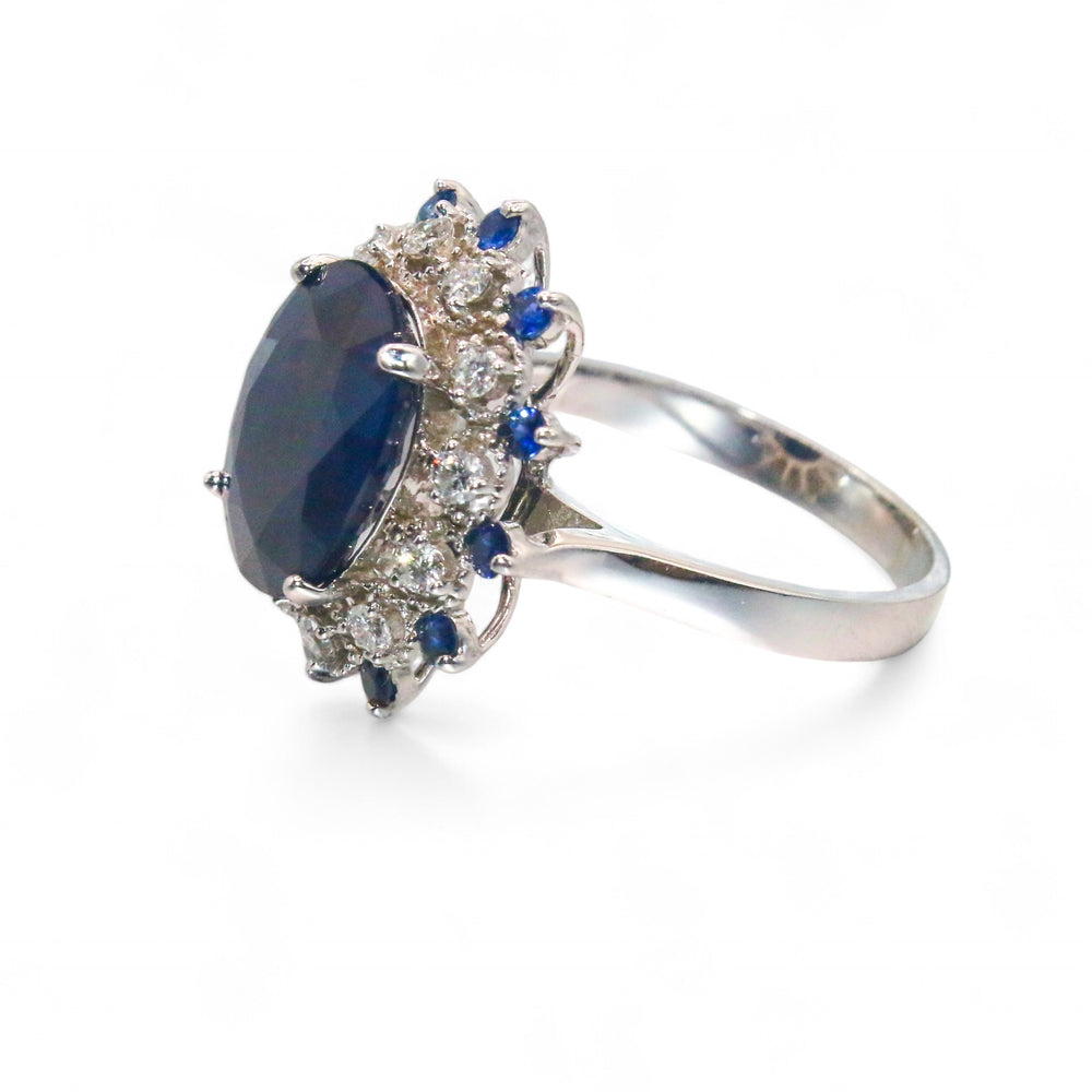 
                  
                    Laurenti Diana Ring featuring an oval blue sapphire surrounded by diamonds and sapphires in 14K white gold.
                  
                