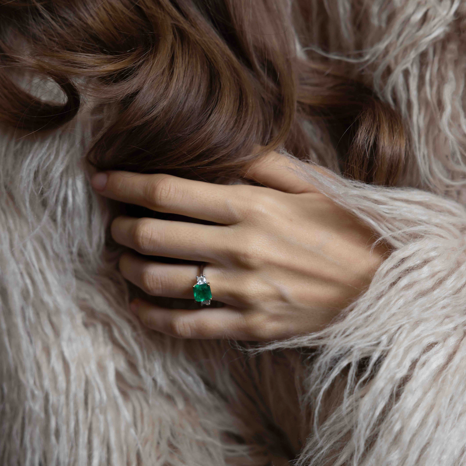 Hand wearing a green gemstone ring on a fluffy beige coat. 