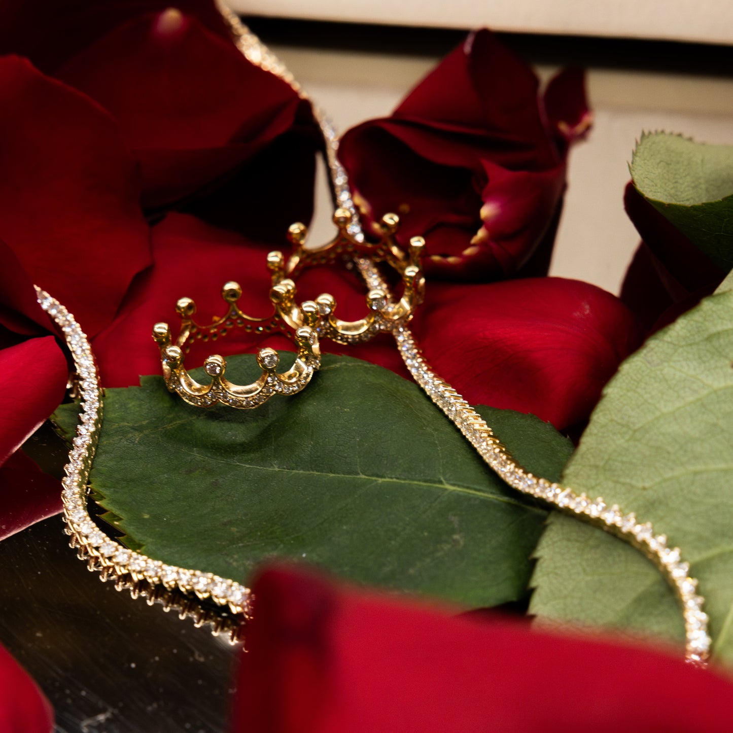 Gold bracelet with crown design on green leaves with red roses