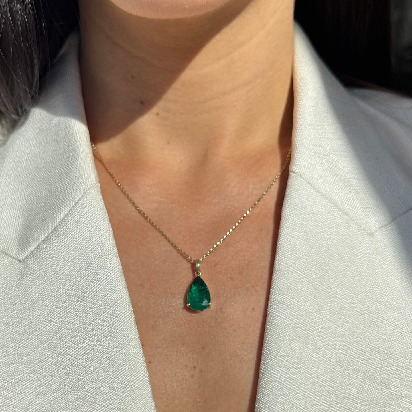 Model wearing a gold necklace with a pear shape emerald pendant.