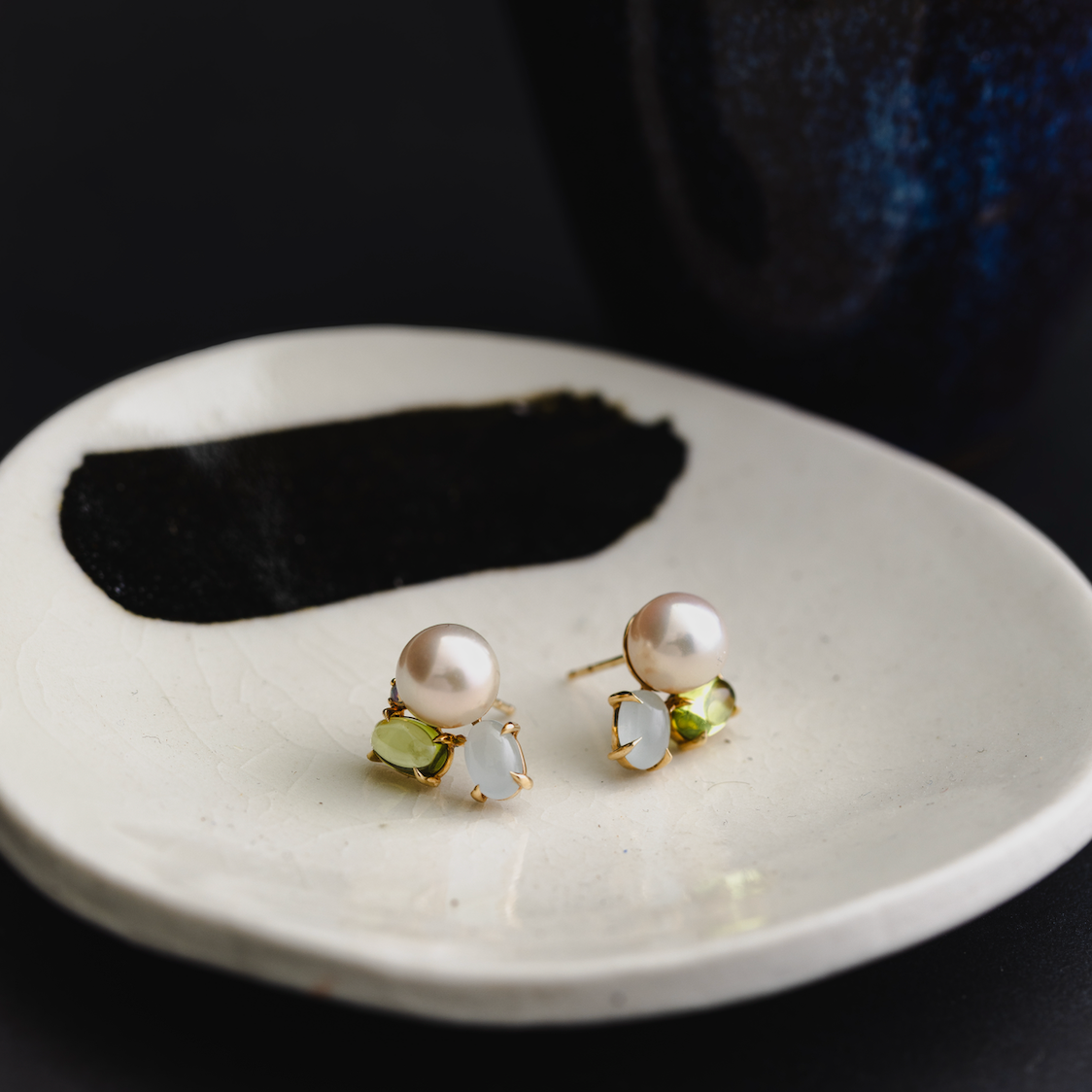 Pearl earrings with green gemstones on a white plate against a dark background