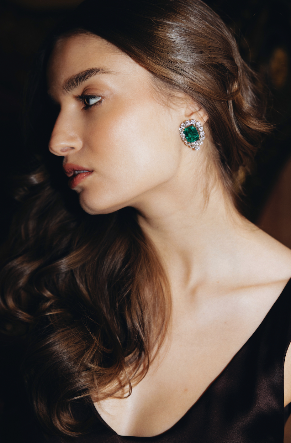 Close-up of a woman wearing emerald green earrings with a dark background